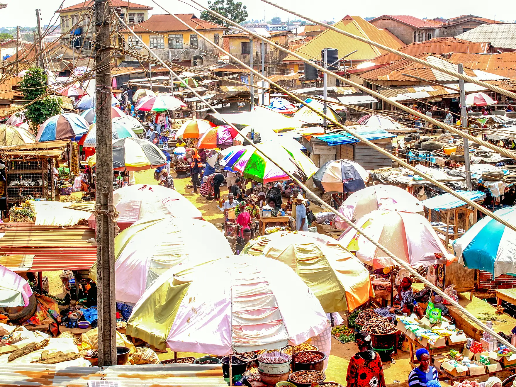 A crowded open-air market in Lagos seen from above, rows of coloured trading umbrellas